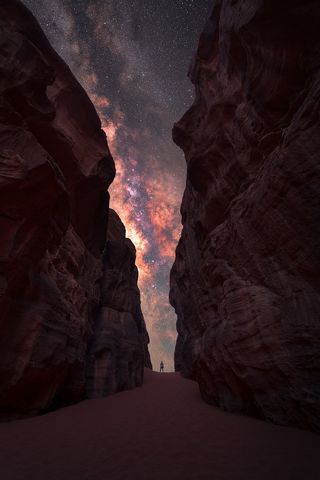 The Milky Way photographed between two tall rocks with a lone man standing in the center